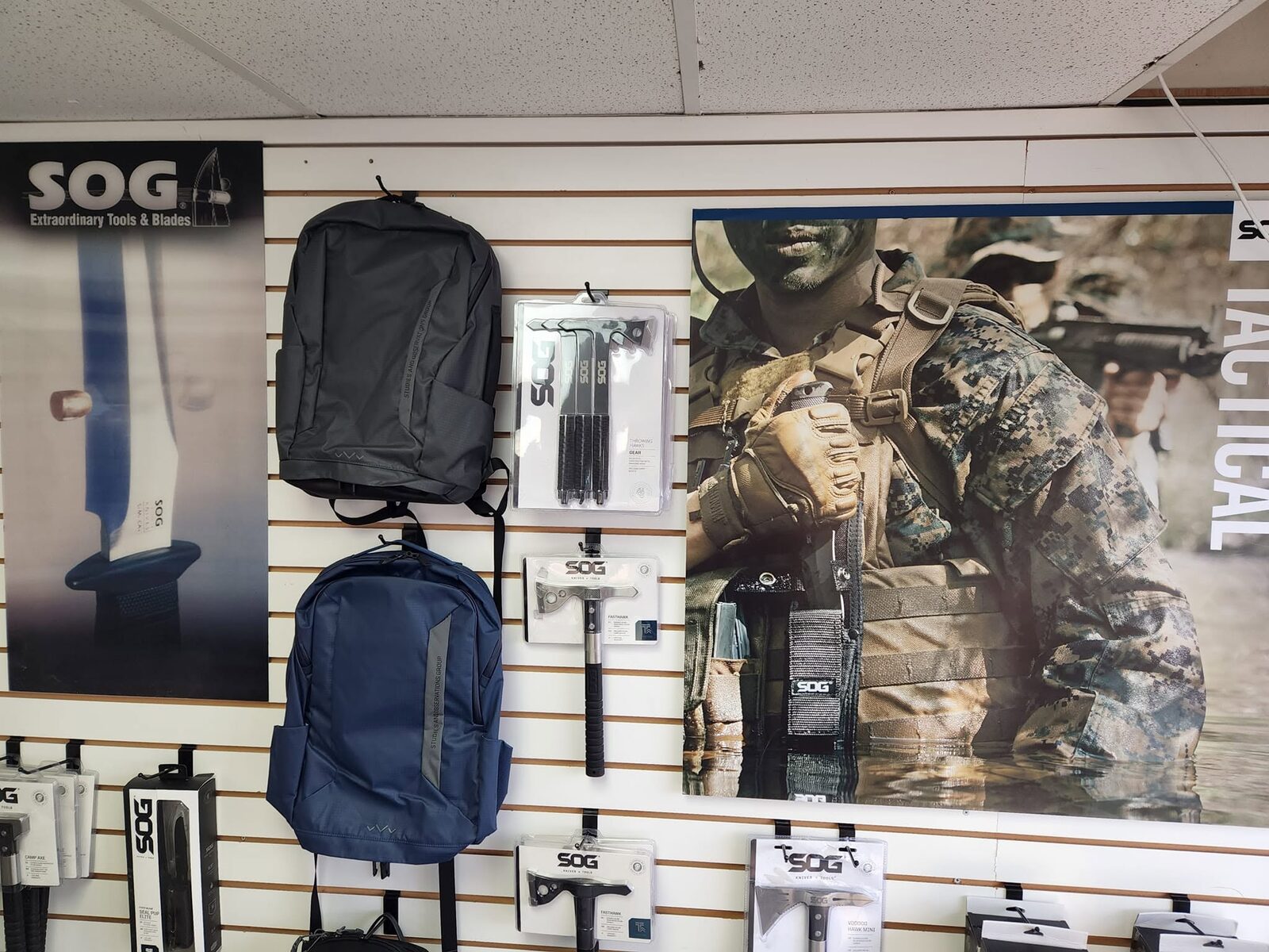 SOG tactical gear, packs, and tomahawks on the shop wall